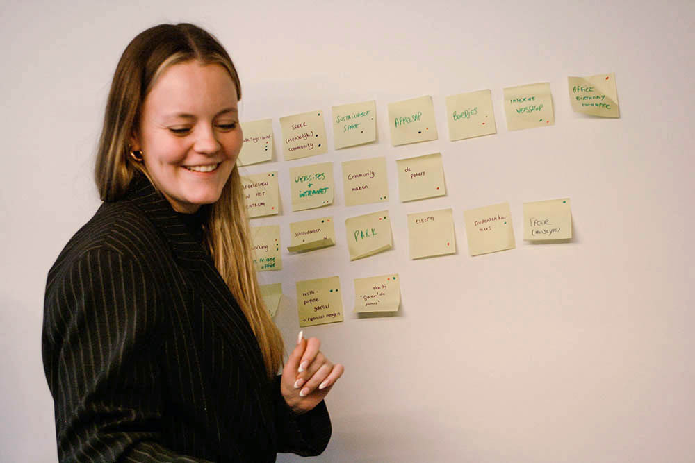BOEM agency frisse blikken Paulien zit in een vergadering en schrijft op post-its enkele gedachten op van de brainstorm, waardoor een beeld ontstaat van de creatieve processen bij BOEM Agency. Het tafereel straalt professionaliteit uit en geeft inzicht in het werk van het bureau.