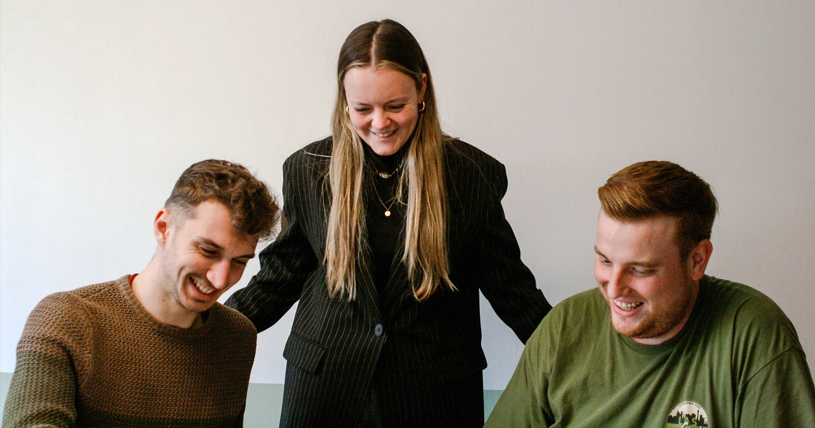 BOEMagency_header_werkenmeteenagency Beeld van een vergadering waar Giel en Dieter zitten terwijl Paulien tussen hen in staat. De sfeer straalt gezelligheid en samenwerking uit, en Paulien lijkt actief betrokken bij het creëren van een positieve en ondersteunende werkomgeving